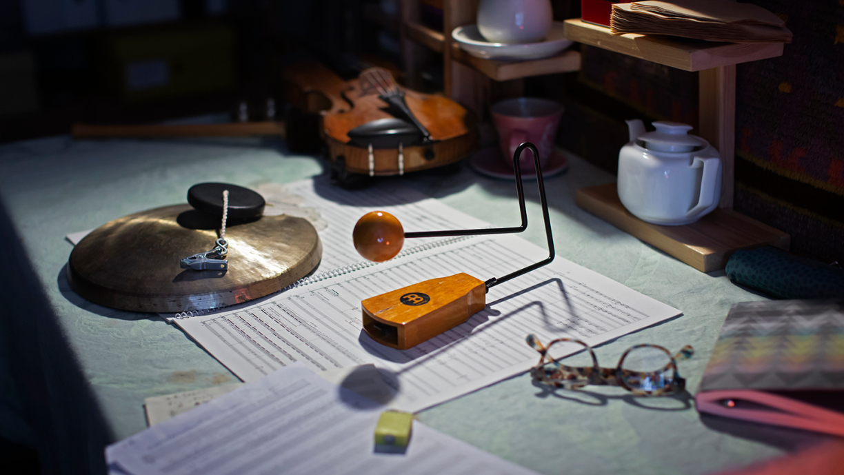 Pöydällä säveltäjän työvälineitä kuten viulu, nuotit ja silmälasit.