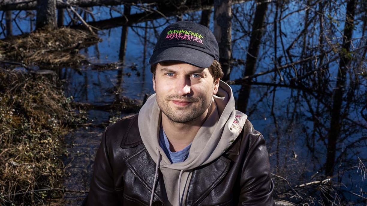 Joel Slotte katsoo kameraan lippalakki päässä. Taustalla näkyy suo.