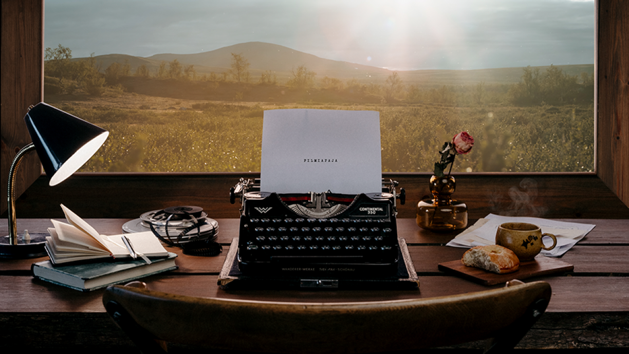 Kirjoituskone tunnelmallisen puurakennuksen sisällä. Kirjoituskoneessa paperiliuska, jossa lukee &quot;Filmiapaja&quot;. Taustalla ikkuna, josta näkyy tunturimaisema.