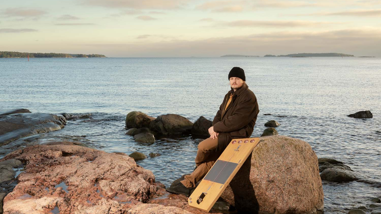 Henkilö istuu rantakiven päällä. Taustalla näkyy järvimaisema.