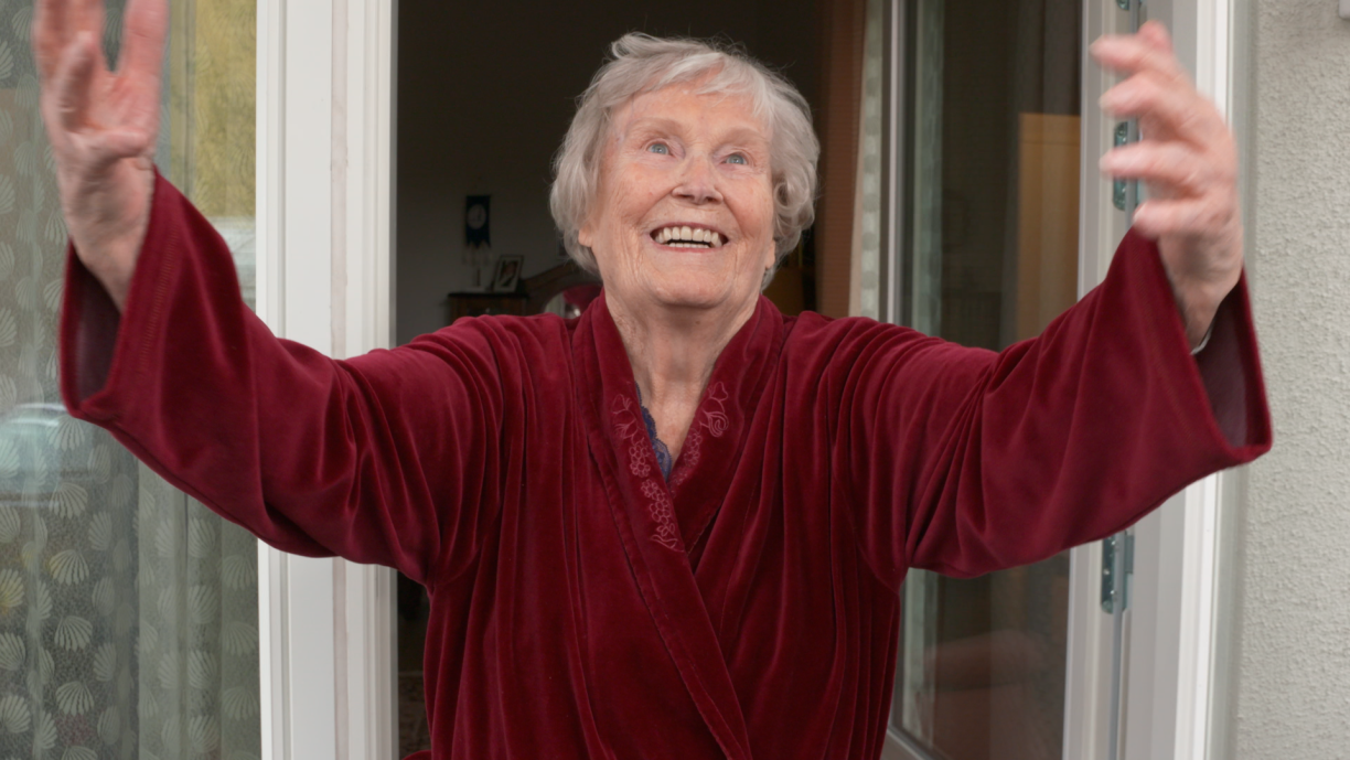 Alina katsoo kameraan ja on nostanut kädet kohti kameraa