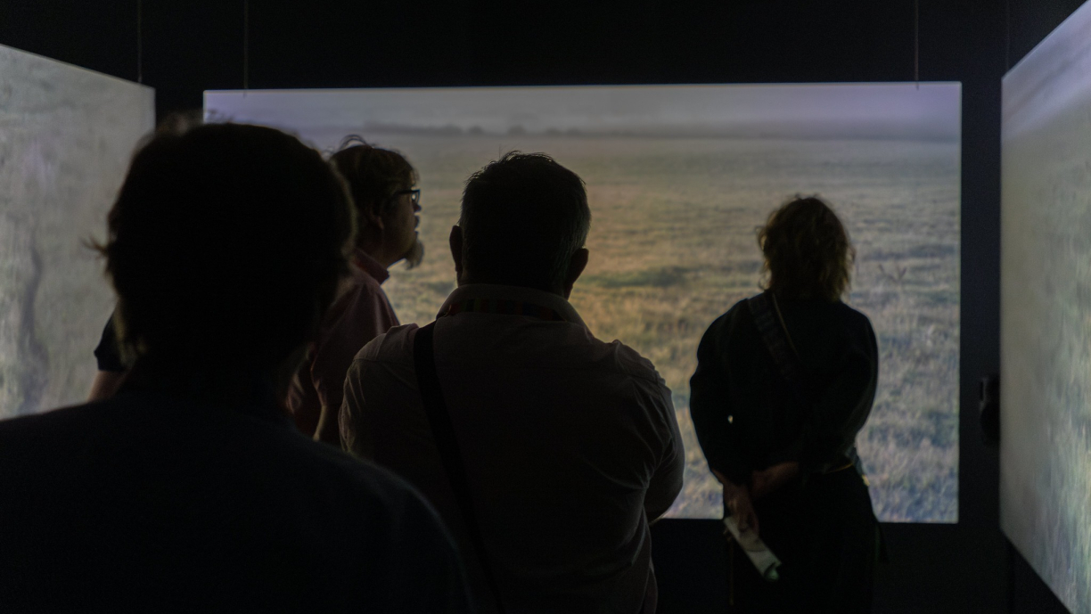 Henkilöt katsovat taustalla näkyvää videoteosta. 