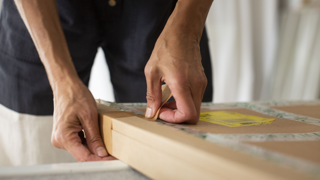 Lähikuva käsistä, jotka teippaavat vanerilaatikkoa kiinni