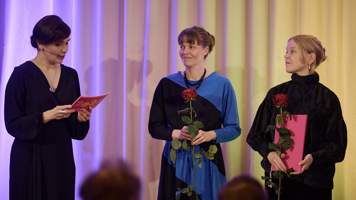 Kaksi henkilöä kuuntelee, kun yksi lukee kortista tekstiä.