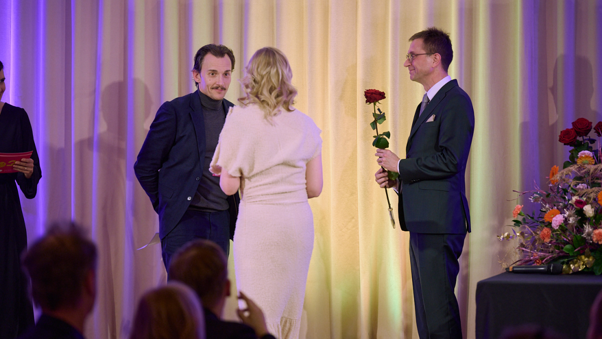 Kaksi henkilöä antavat palkintoa kolmannelle henkilölle.