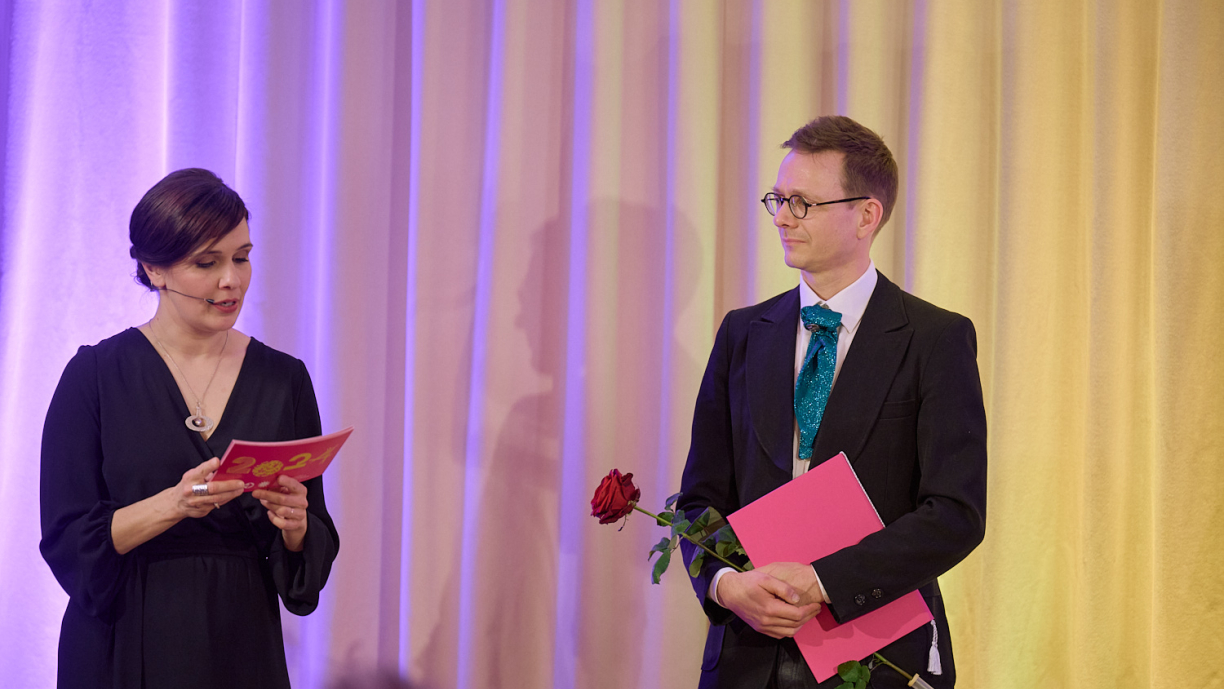 Toinen henkilö lukee paperista ja toinen henkilö kuuntelee katsellen häntä.