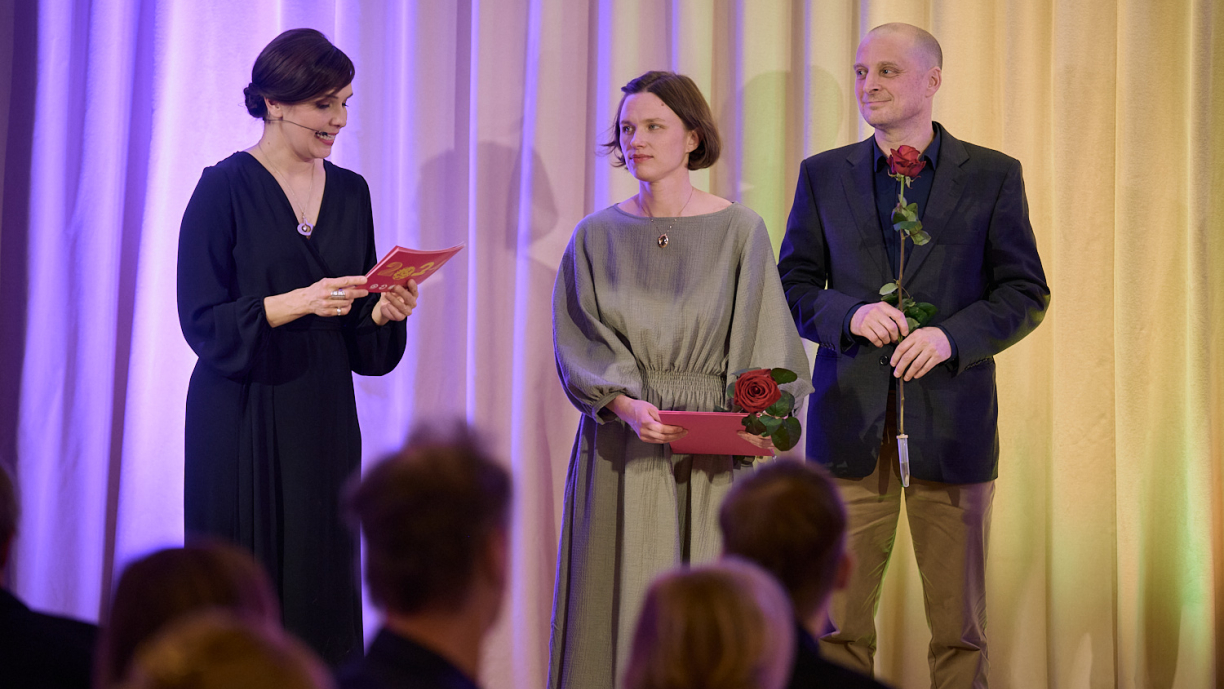 Kaksi henkilöä kuuntelee, kun kolmas lukee kortista tekstiä.