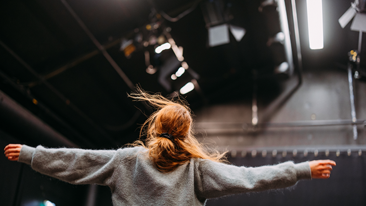 Tanssija selkä katsojaa kohti kädet levitettynä sivuille.