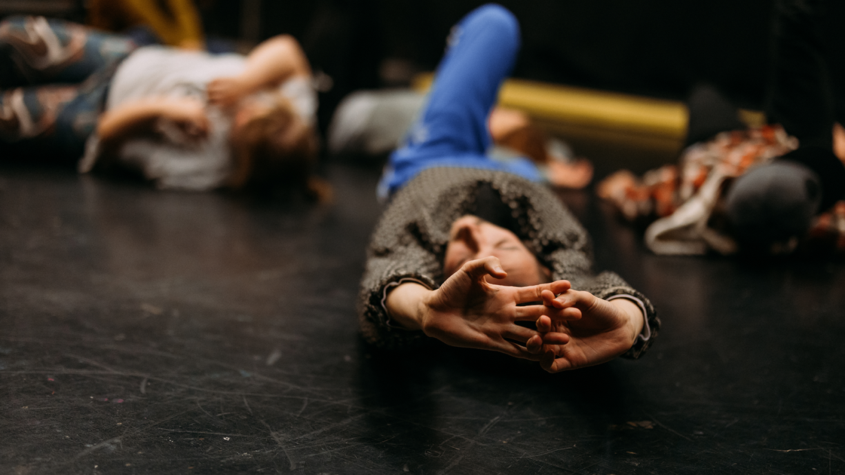 Ihmisiä makoilemassa mustalla lattialla.