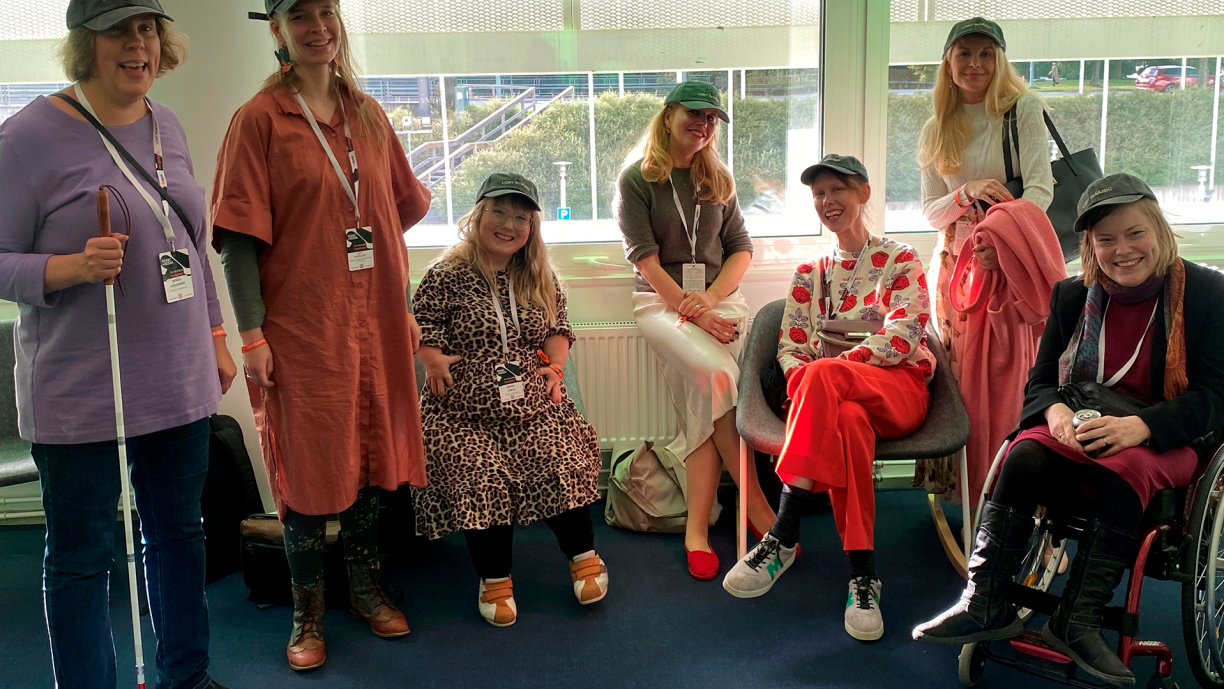 Ihmisiä ikkunan edessä katsomassa kameraan.