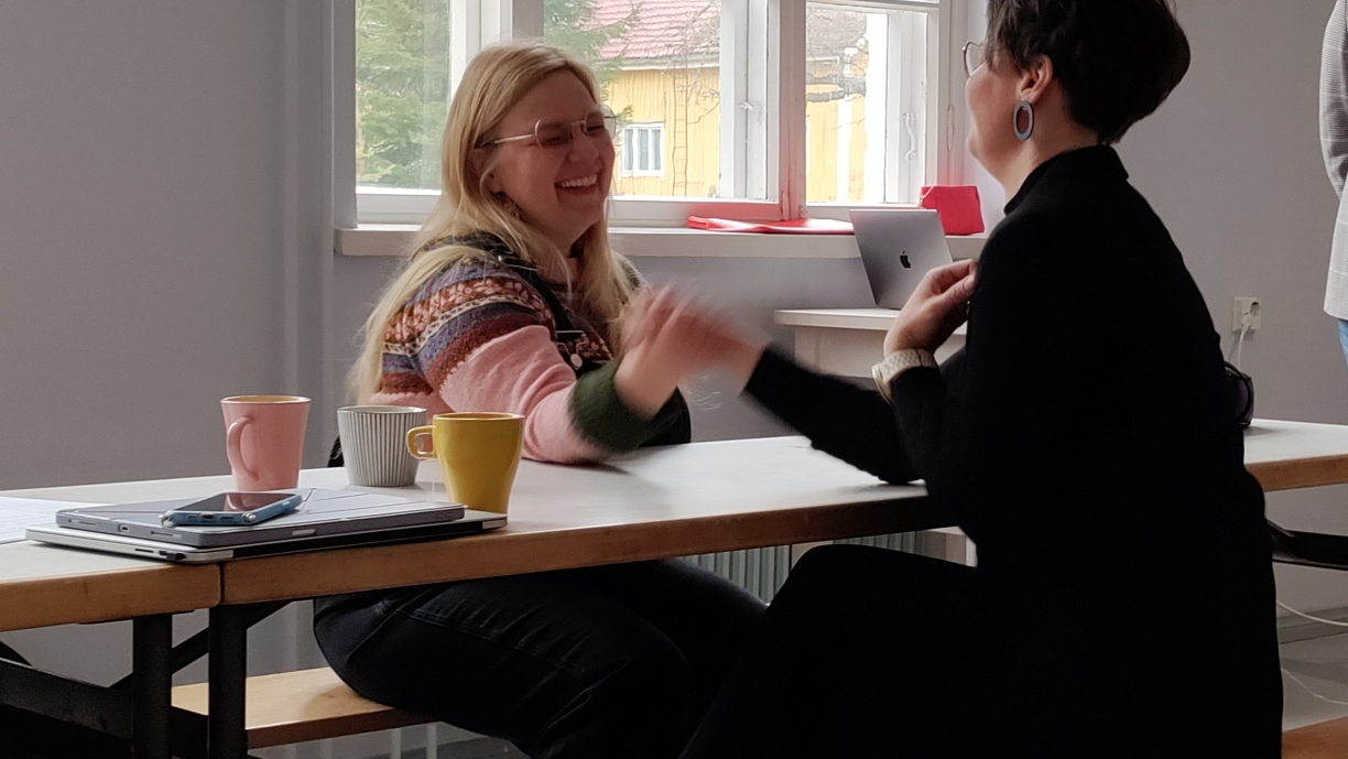 Rento tilannekuva nauravista Tiina Purasesta ja Susanna Mäki-Oversteynsista Lottaliina Pokkisen työpajassa vääntämässä pöydän ympärillä kahvikuppien kanssa.
