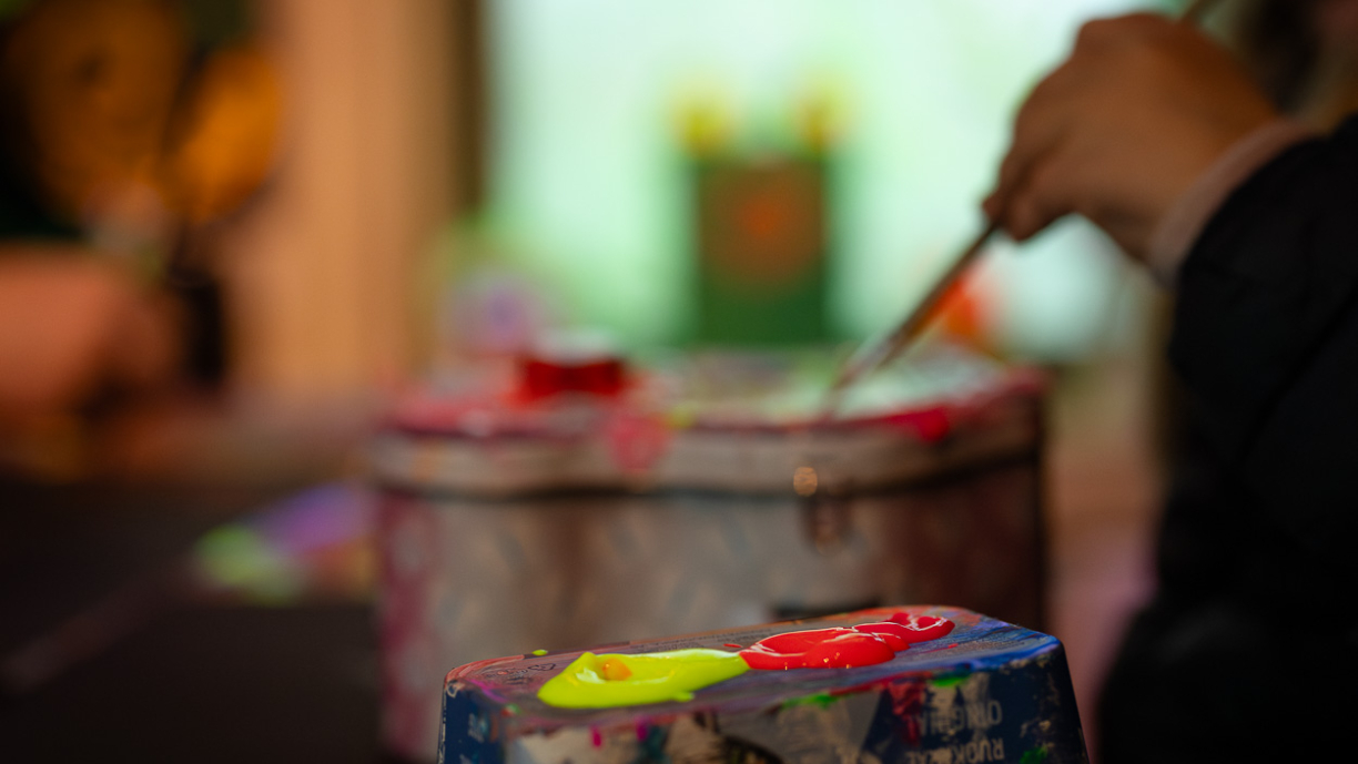 Keltaista ja punaista maalia sekoitusalustalla. Taustalla pensseli.