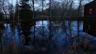 Maalaismaiseman keskellä oleva lampi pimenevässä illassa. Lammenpintaan on heijastettu teksti "Tulet, jäät."