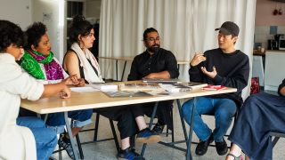 Taideyhteisön jäsenet keskustelevat pöydän ympärillä.