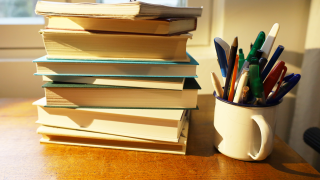 Kirjapino pöydällä ja vieressä purkki, jossa on kyniä