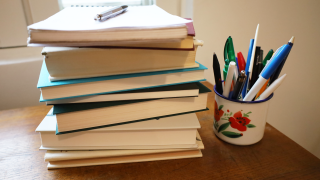 Kirjapino pöydällä ja vieressä purkki, jossa on kyniä