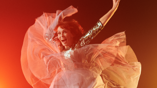 Tanssija hyppää ilmaan esityksessä ja hänen mekkonsa helmat lentävät.