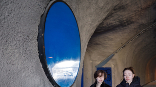 Kaksi henkilöä kävelee seinämässä olevan julkisen taideteoksen ohi.