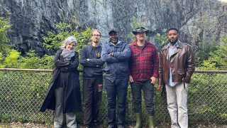 Viisi ihmistä seisoo rivissä, taustalla louhos.