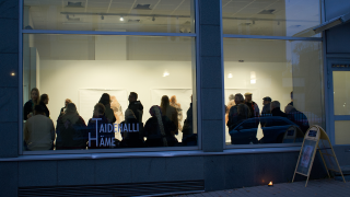 Ihmisiä galleriassa kuvattuna ikkunan ulkopuolelta.