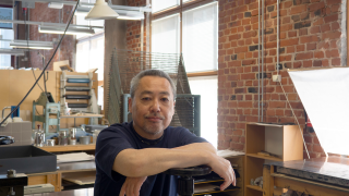 Naoji Ishiyama istuu työhuoneessaan ja katsoo kameraan.