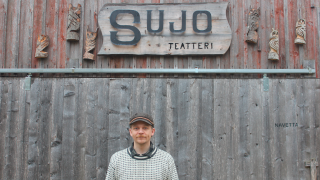 Henkilö seisoo puutalon edessä.