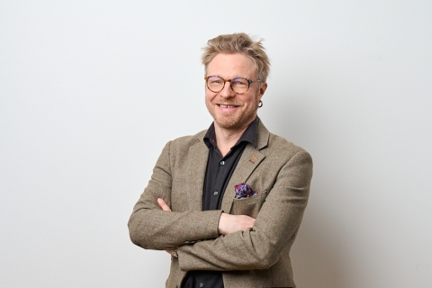 Hymyilevä kasvokuva Tuomas Korkalosta vaaleaa seinää vasten.