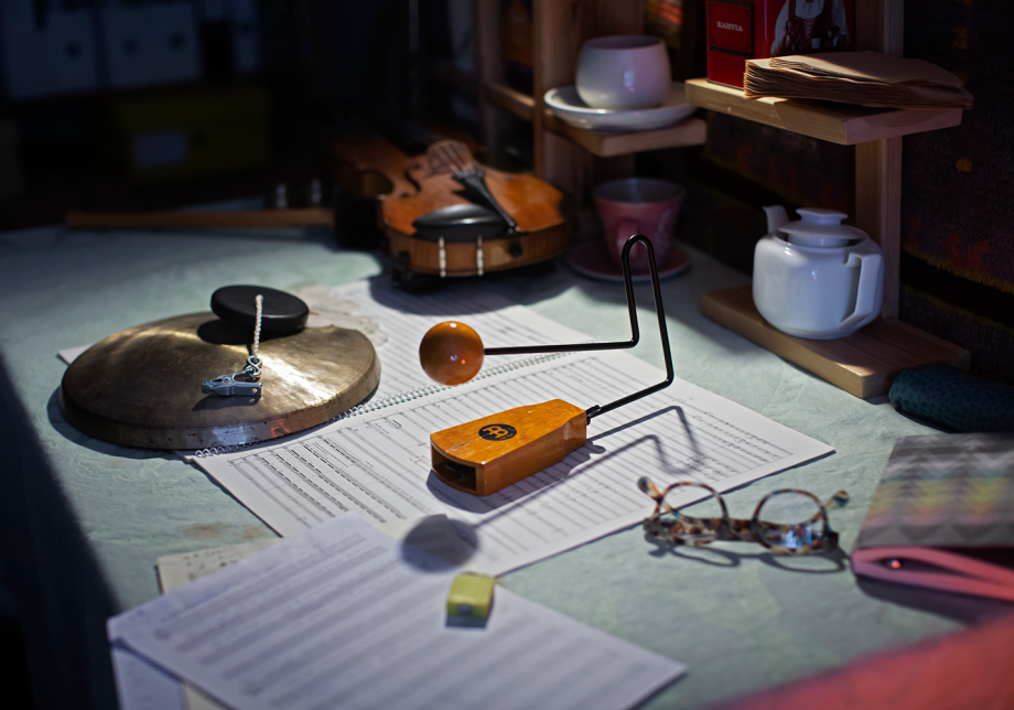Pöydällä säveltäjän työvälineitä kuten viulu, nuotit ja silmälasit.