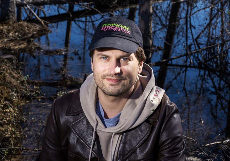 Joel Slotte katsoo kameraan lippalakki päässä. Taustalla näkyy suo.