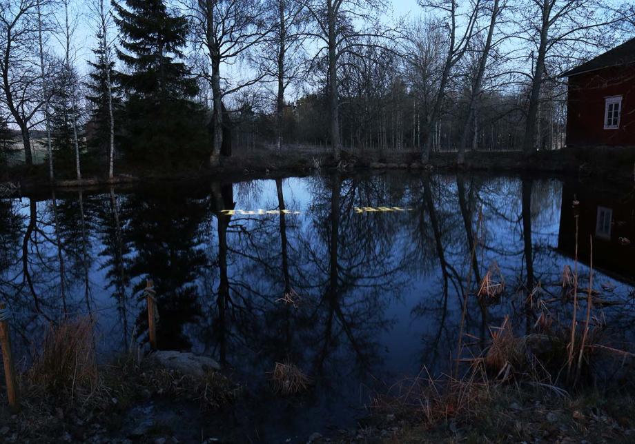 Maalaismaiseman keskellä oleva lampi pimenevässä illassa. Lammenpintaan on heijastettu teksti "Tulet, jäät."