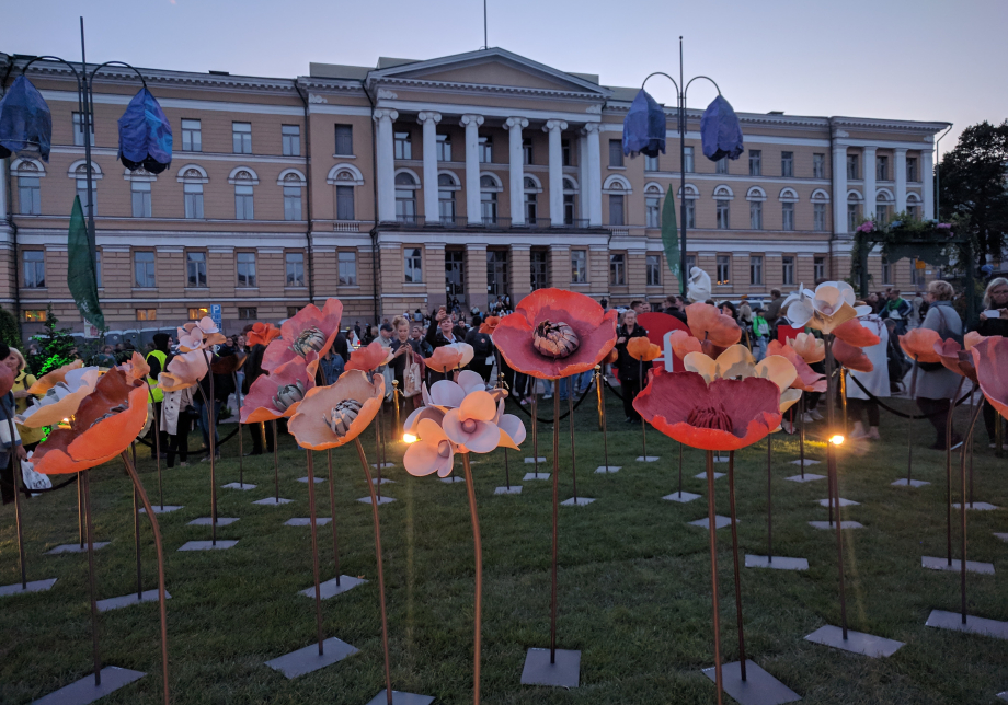 Helsingin Senaatintorilla ihmisiä kerääntyneenä suurten jalustoilla seisovien kukkaveistosten luokse.