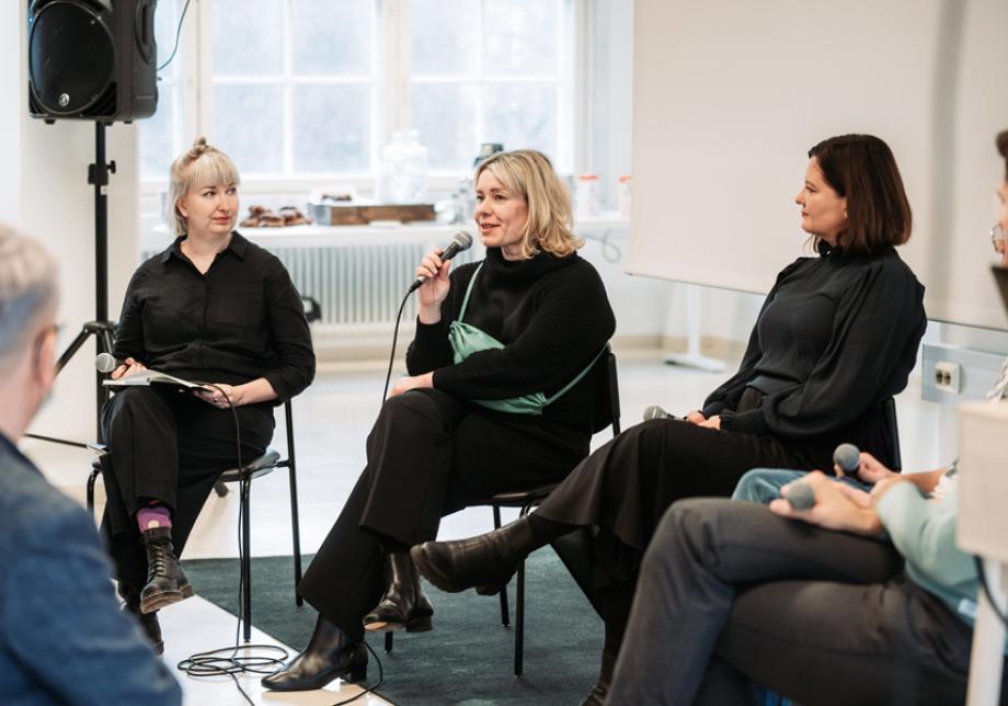 Kolme henkilöä istuu keskustelemassa yleisön edessä