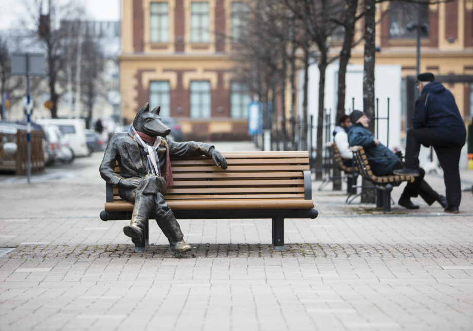 Veistos, jossa susihahmo istuu ulkona penkillä 