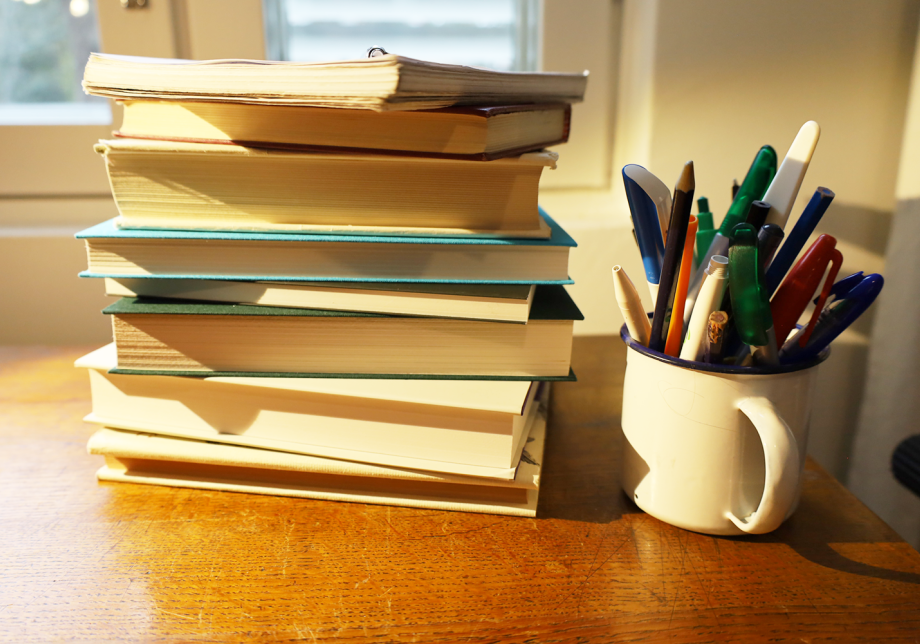 Kirjapino pöydällä ja vieressä purkki, jossa on kyniä