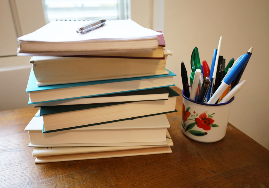 Kirjapino pöydällä ja vieressä purkki, jossa on kyniä