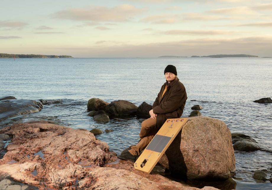 Henkilö istuu rantakiven päällä. Taustalla näkyy järvimaisema.