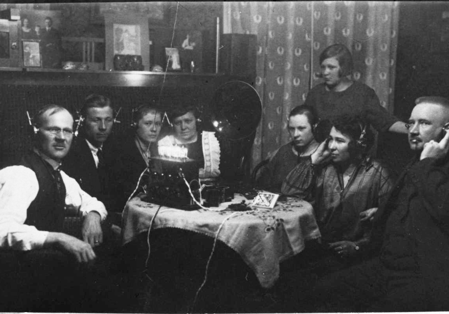 Ihmisiä istumassa pöydän ympärillä kuuntelemassa radiota korvakuulokkeilla