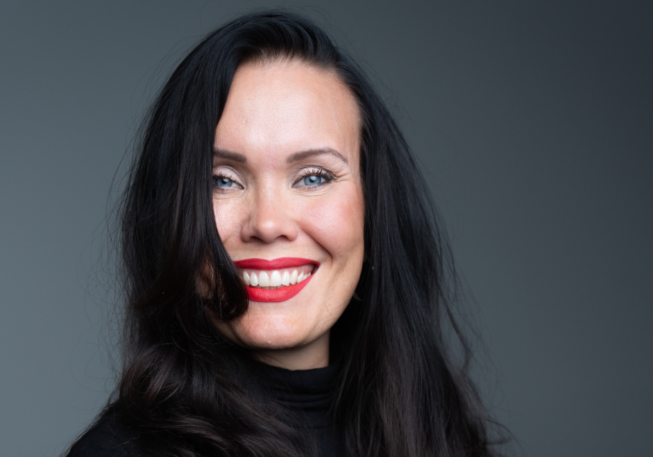 Katriina Haikala puolikuvassa harmaan taustan edessä musta paita yllään