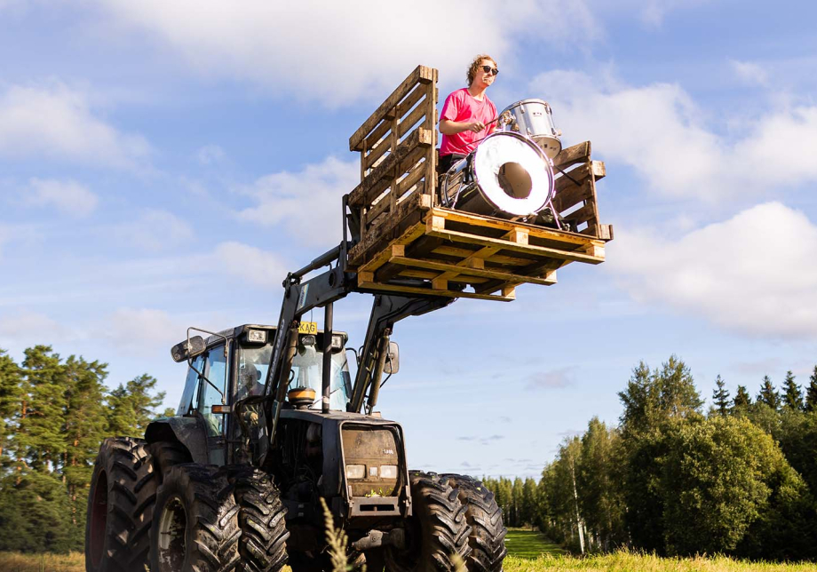 Henkilö soittaa rumpuja traktorin haarukkanostimessa.