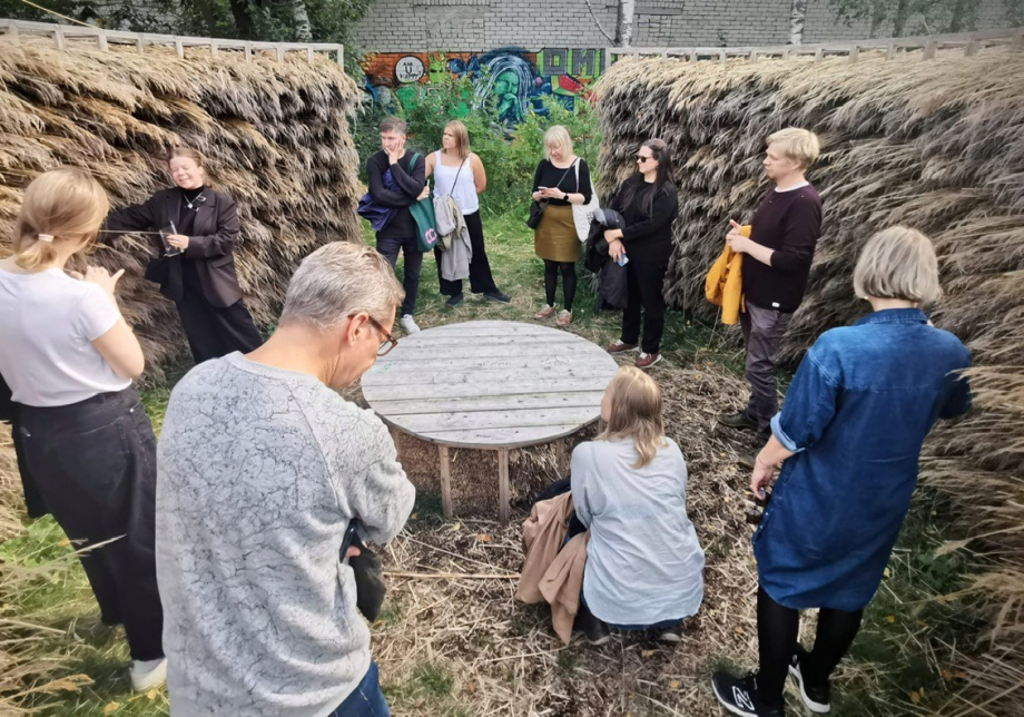 Ihmisiä kerääntyneenä kuuntelemaan opastusta heinästä muodostetun seinämän sisäpuolelle.