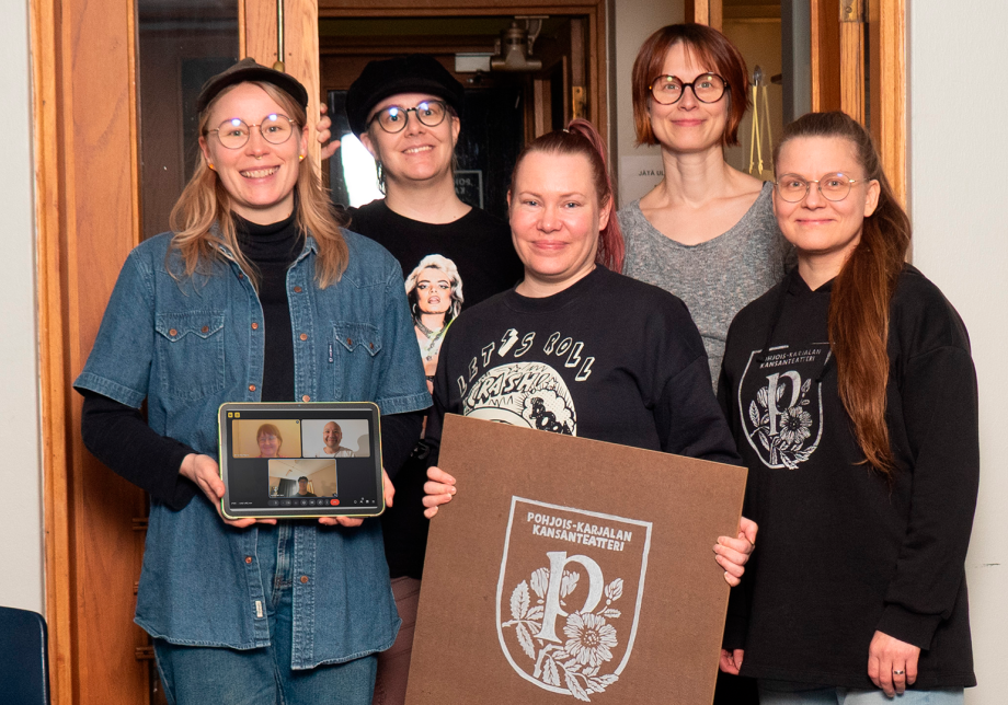 Viisi ihmistä seisoo muodostelmassa ja yhdellä on kädessään kyltti.