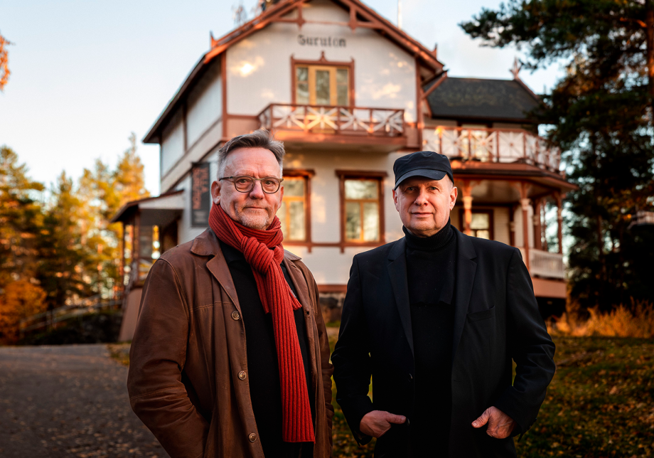 Kaksi henkilöä seisoo puutalon edessä.