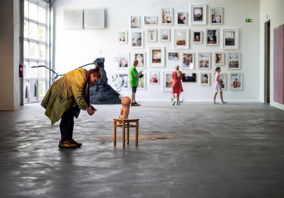 Taidenäyttelyn kävijä katselee lähietäisyydeltä pientä puista veistosta