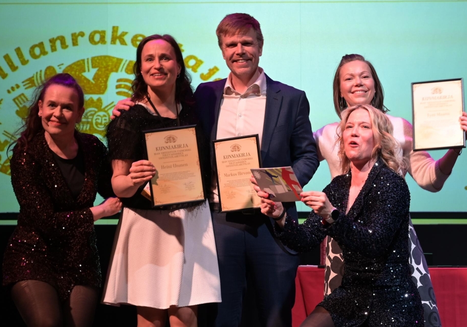 Maakuntajohtajat seisovat kunniakirjat käsissään. Sillanrakentajien Virpi ja Tiia-Mari ovat reunoilla glitter-mekoissa.