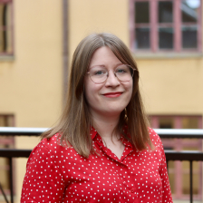 Henkilö hymyilee kaiteen edessä.