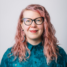 Kasvokuva Satu Kokkoniemestä vaalealla taustalla. Satu hymyilee ja hänellä on kuvioitu turkoosi kauluspaita.