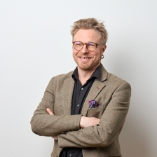 Hymyilevä kasvokuva Tuomas Korkalosta vaaleaa seinää vasten.